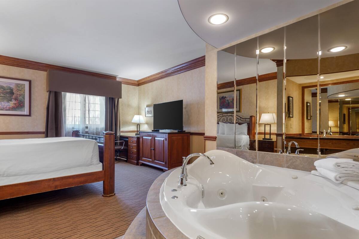 A hotel room with a large bed, a separate bathroom with a bathtub, a television, and a large mirror.