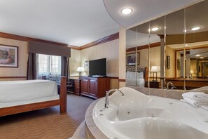 A hotel room with a large bed, a separate bathroom with a bathtub, a television, and a large mirror.