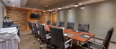 A conference room with a long table, multiple chairs, a TV mounted on the wall, and a stone accent wall.