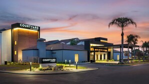 A Courtyard by Marriott hotel with a modern design, a well-lit entrance, and a landscaped area with palm trees. - Courtyard by Marriott Fresno (Fresno)