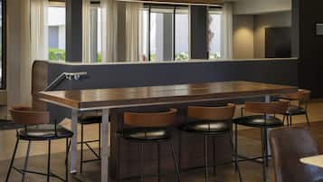 Un área de bar moderna con una mesa de madera alargada, seis taburetes de cuero negro y ventanas amplias con cortinas.