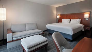 A hotel room with a bed, a sofa, a chair, a table, and a lamp.