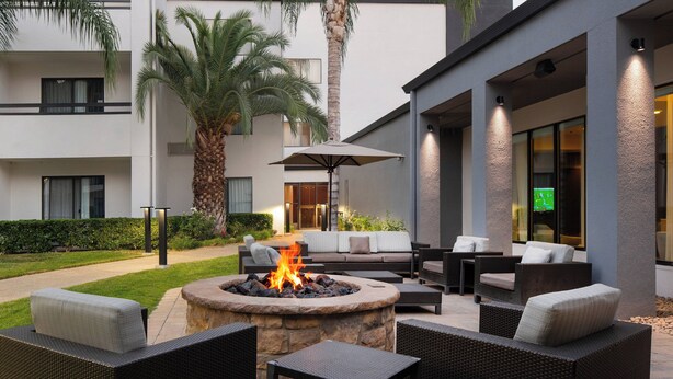 An outdoor patio area with a stone fire pit, wicker furniture, and a sofa with cushions. - Courtyard by Marriott Fresno (Fresno)