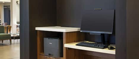 A modern office desk with a computer, keyboard, and mouse, a printer, and a dark-colored wall.