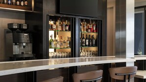 A bar area with a coffee machine, shelves of liquor bottles, and two bar stools. - Courtyard by Marriott Fresno (Fresno)