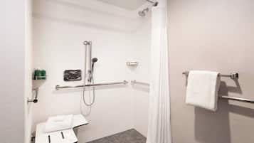 A small, accessible shower room with a white towel, a shelf with toiletries, and a grab bar.