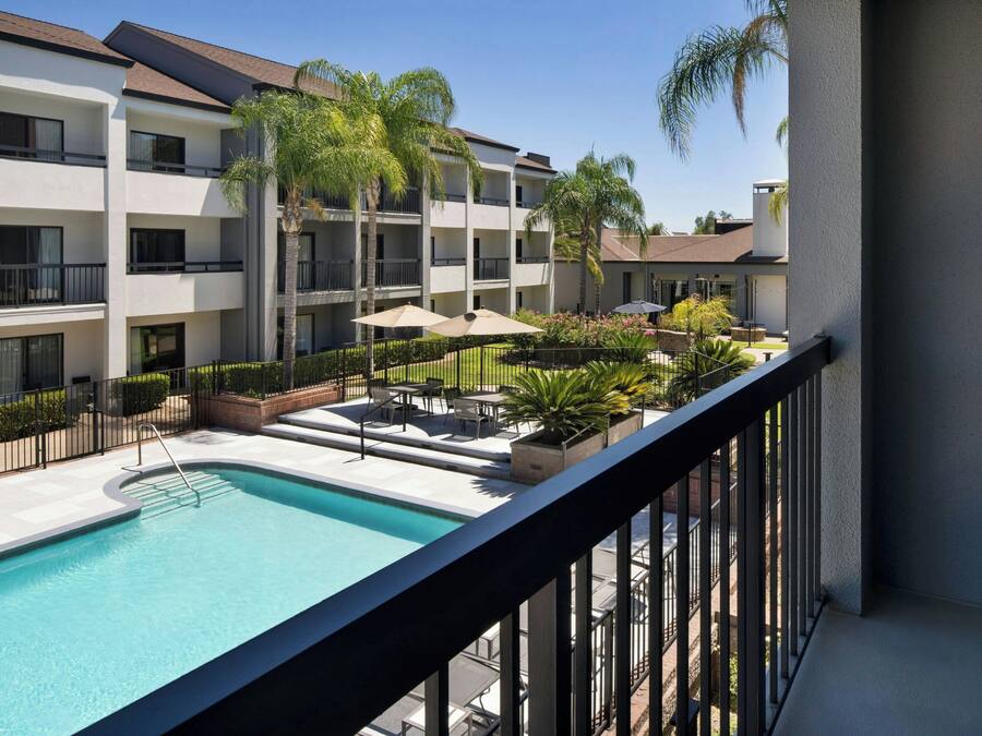 A hotel courtyard with a swimming pool, outdoor seating, and palm trees.