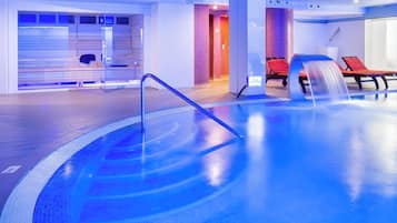 Une piscine intérieure moderne dotée d’un bassin à eau cristalline, de chaises longues et d’un espace spa clos par des parois de verre.
