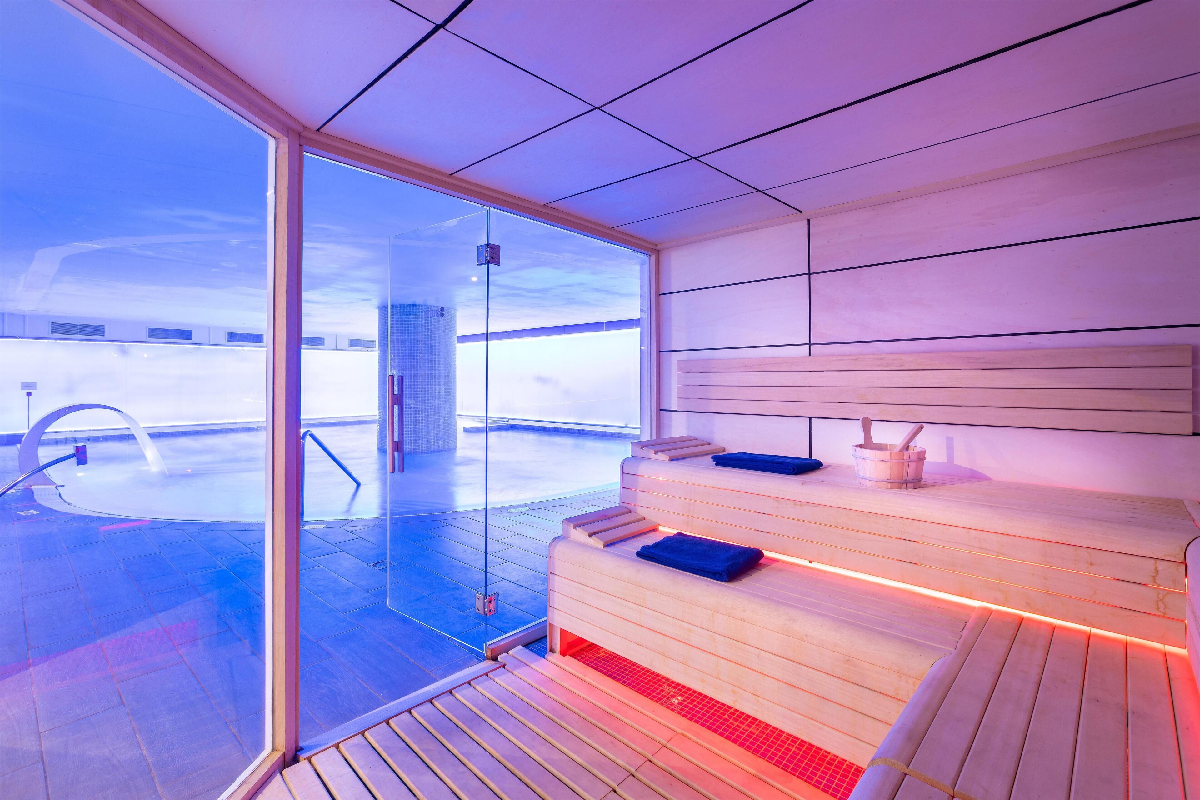 Una sauna moderna con puerta de cristal, bancos de madera y vistas a un paisaje nevado.