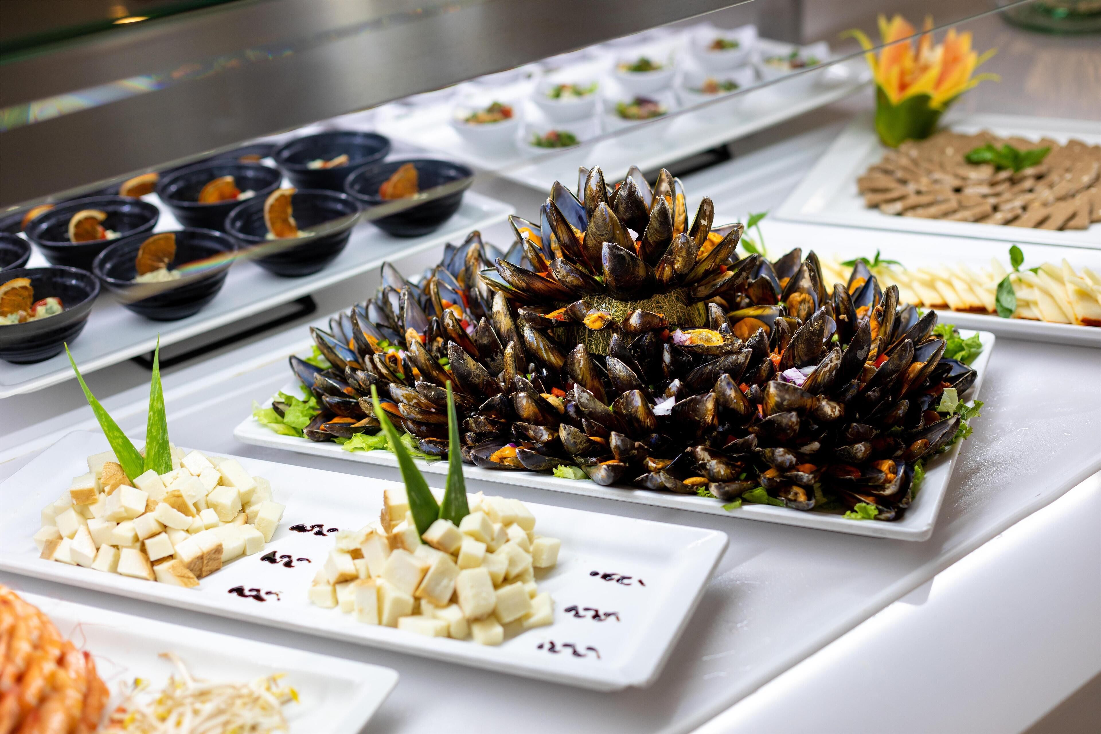 Un bufé con diversos platos, entre ellos mejillones, tofu y otros alimentos preparados.