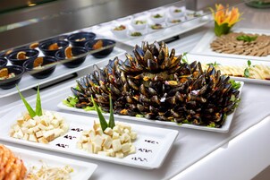 Un bufé con diversos platos, entre ellos mejillones, tofu y otros alimentos preparados.
