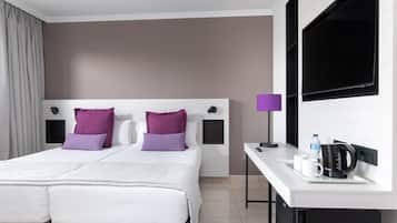 Quarto de hotel com cama de casal, escrivaninha com cafeteira e televisão.