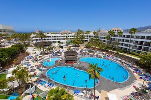 Um resort com várias piscinas, palmeiras e vista para o oceano.