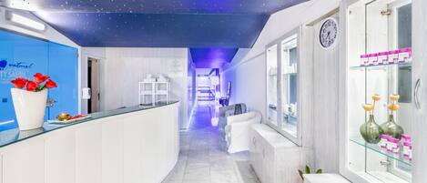 Een moderne hotel lobby met een gebogen receptiebalie, een klok aan de muur en een blauw plafond met sterachtige lampen.