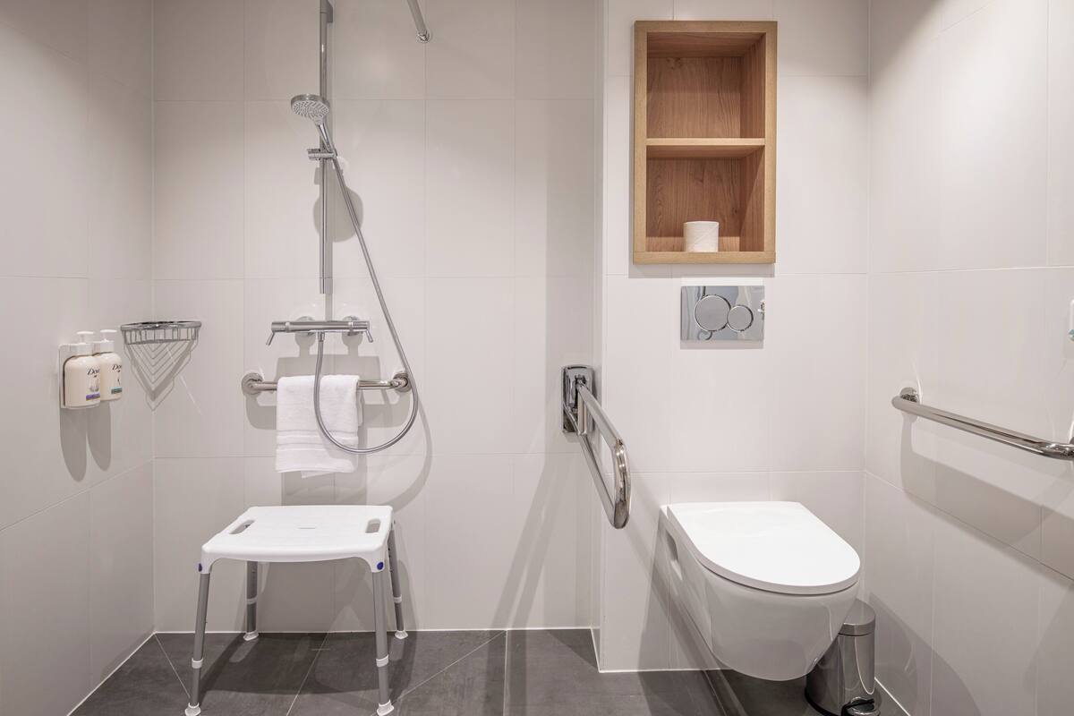 A modern bathroom with a shower, toilet, and grab bars.