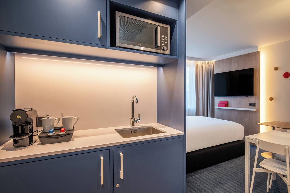 A compact hotel room with a kitchenette, a bed, a TV, and a small table.