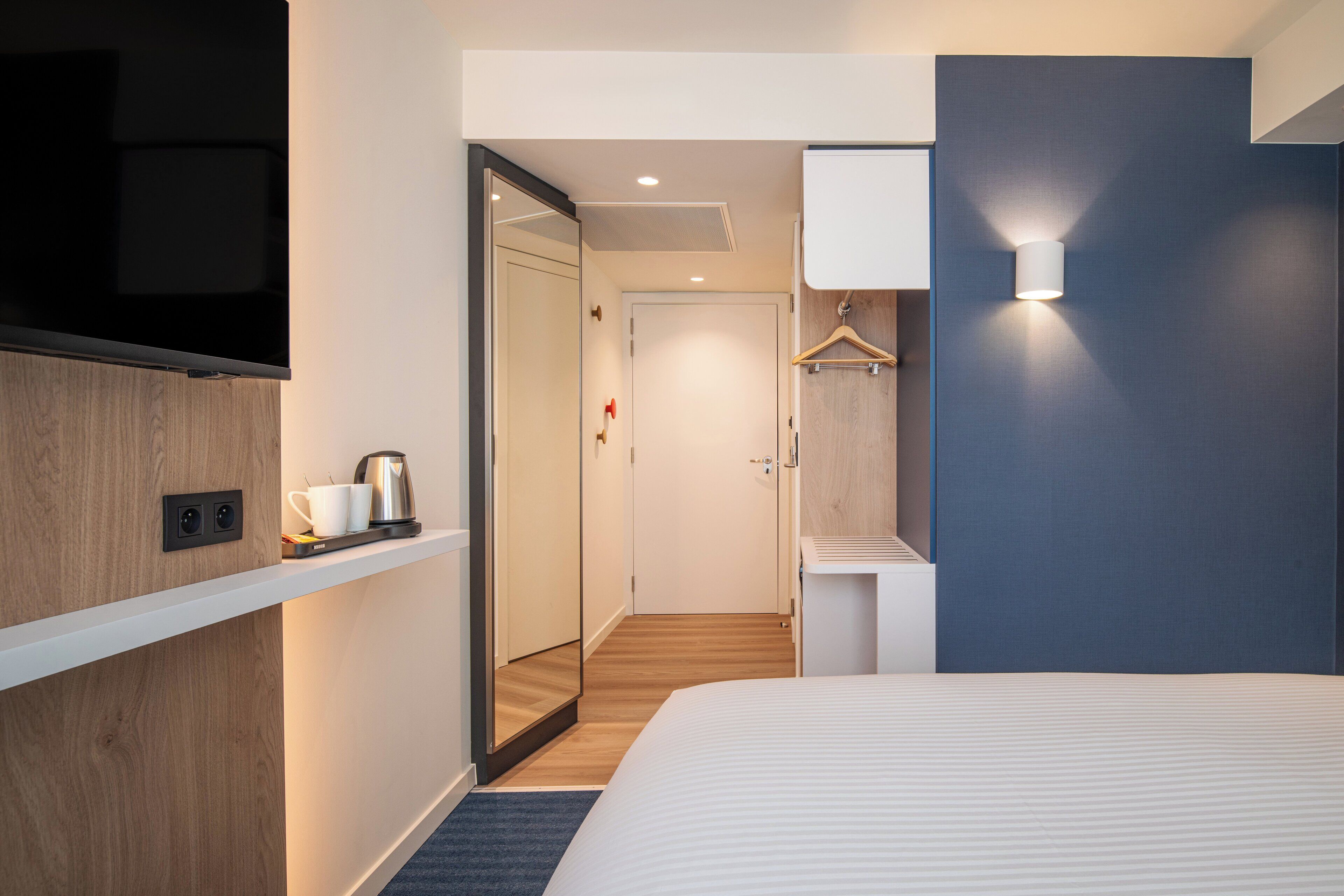 A modern hotel room with a large bed, a flat-screen TV, a coffee maker, and a wardrobe.