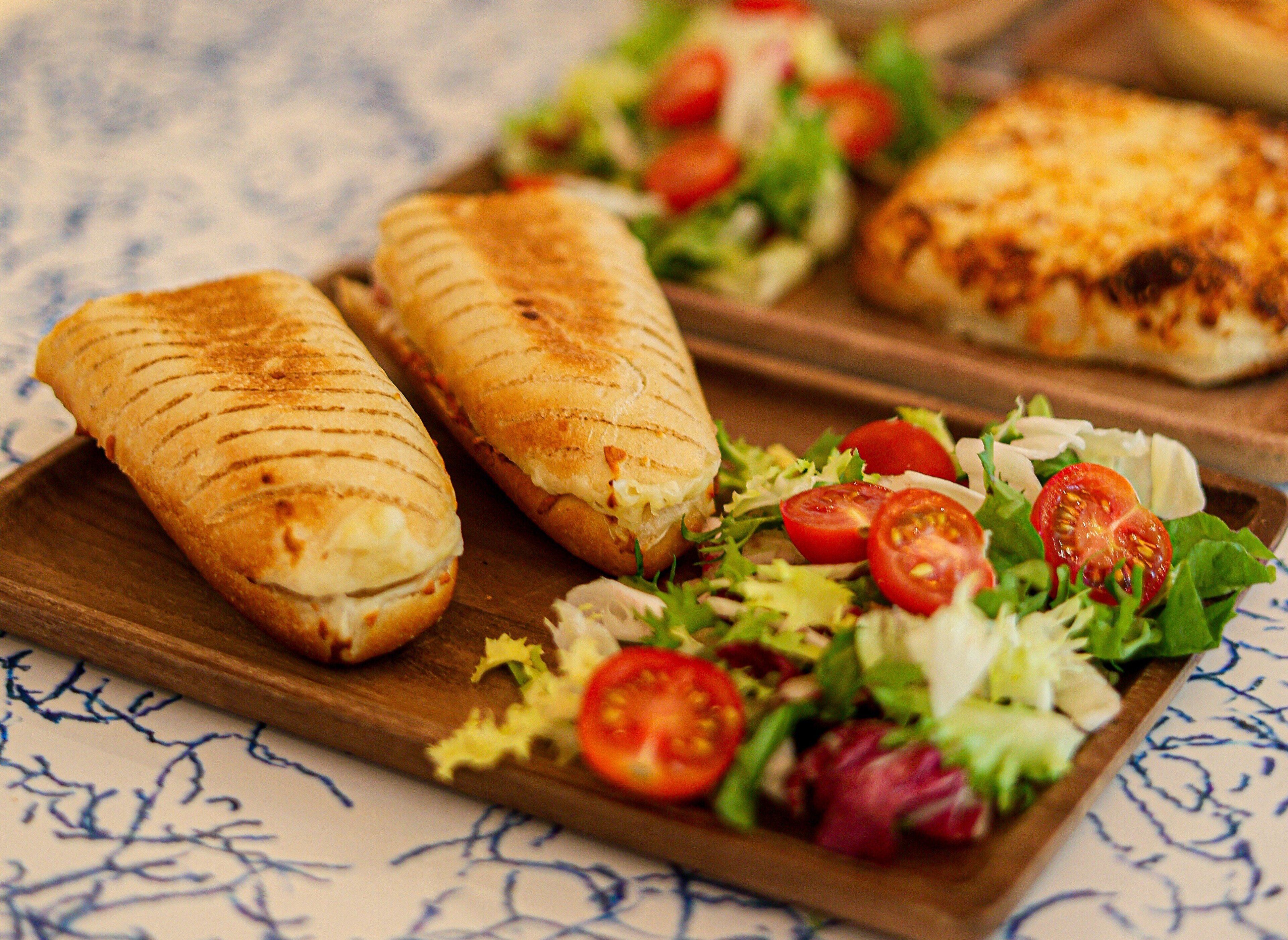 Una tabla de madera con sándwiches a la parrilla y una ensalada fresca con tomates y lechuga.