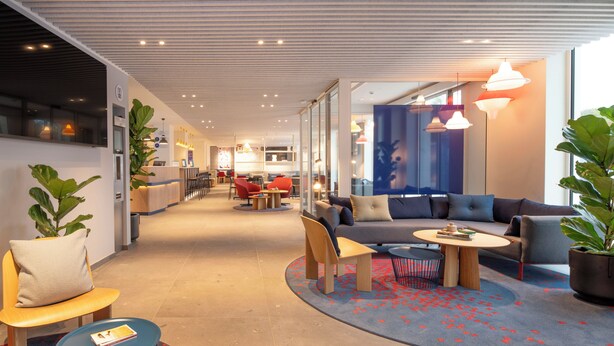 A modern interior with a reception desk, seating area, and a kitchen in the background. - Holiday Inn Express & Suites Ghent by IHG (Ghent)