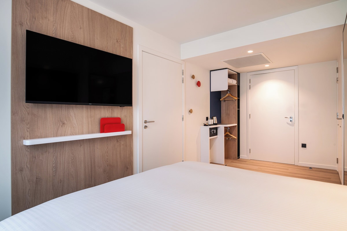 A modern bedroom with a large bed, a mounted TV, and a wardrobe with a mirror.