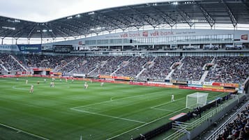 A stadium with multiple tiers of seating, a large field, and advertisements for VDK Bank and Play Sports.