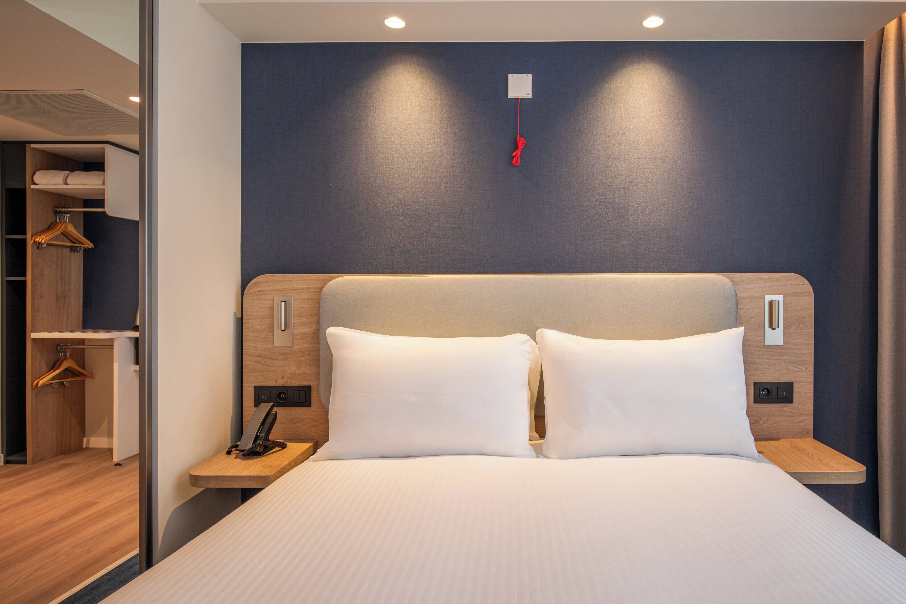Habitación de hotel con una cama grande, cabecero de madera, mesitas de noche y un armario con ropa colgada.