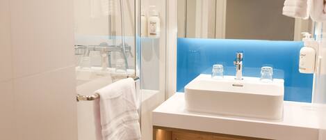 Un baño moderno con cabina de ducha de vidrio, un lavabo blanco con estante de madera y una pared de acento azul.