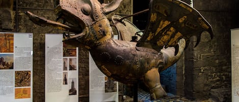 A historical exhibit featuring a large, ornate, metallic sculpture of a mythical creature, displayed in a museum with informational panels and a patterned floor.
