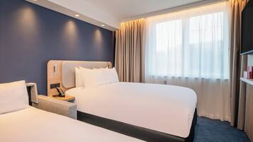 A hotel room with two beds, a nightstand, a desk, and a large window with curtains.