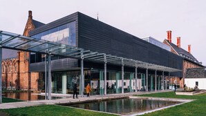A modern building with a glass facade, a courtyard with a water feature, and a traditional brick structure in the background. - Holiday Inn Express & Suites Ghent by IHG (Ghent)