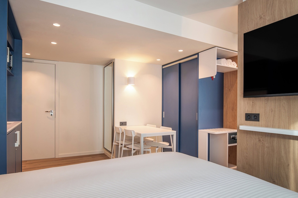 A modern hotel room with a bed, a desk, and a TV.