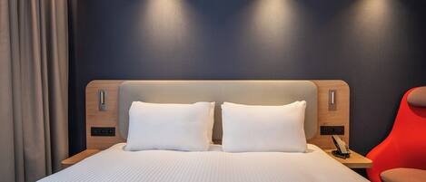 Una habitación de hotel moderna con una cama grande, cabecera de madera, una silla roja y una pared oscura.