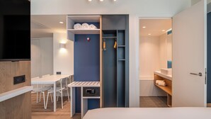 A modern hotel room with a bed, a desk with chairs, a wardrobe, and a bathroom with a bathtub and shelves. - Holiday Inn Express & Suites Ghent by IHG (Ghent)