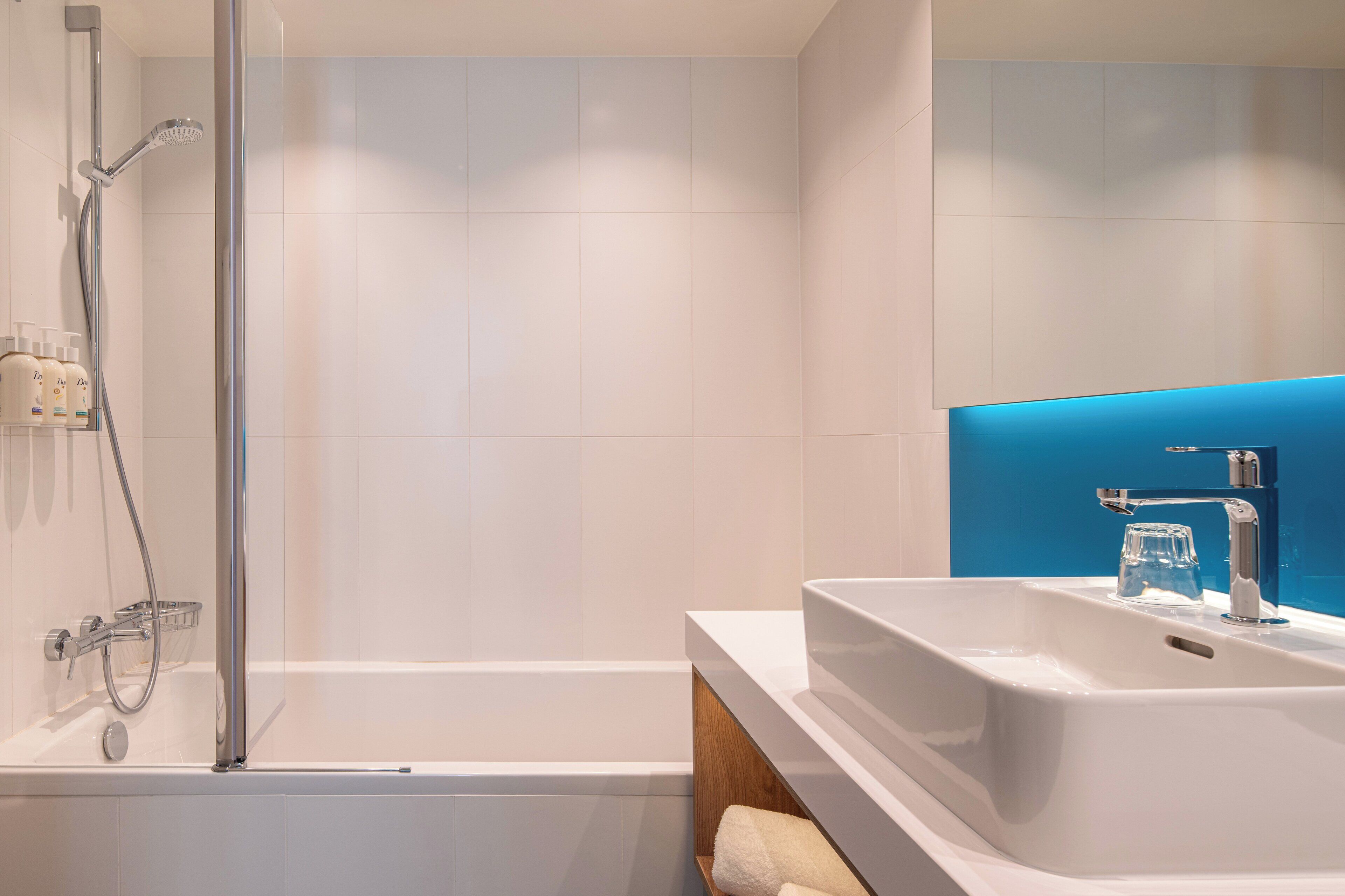 A modern bathroom with a bathtub, a shower, and a sink with a blue accent wall.