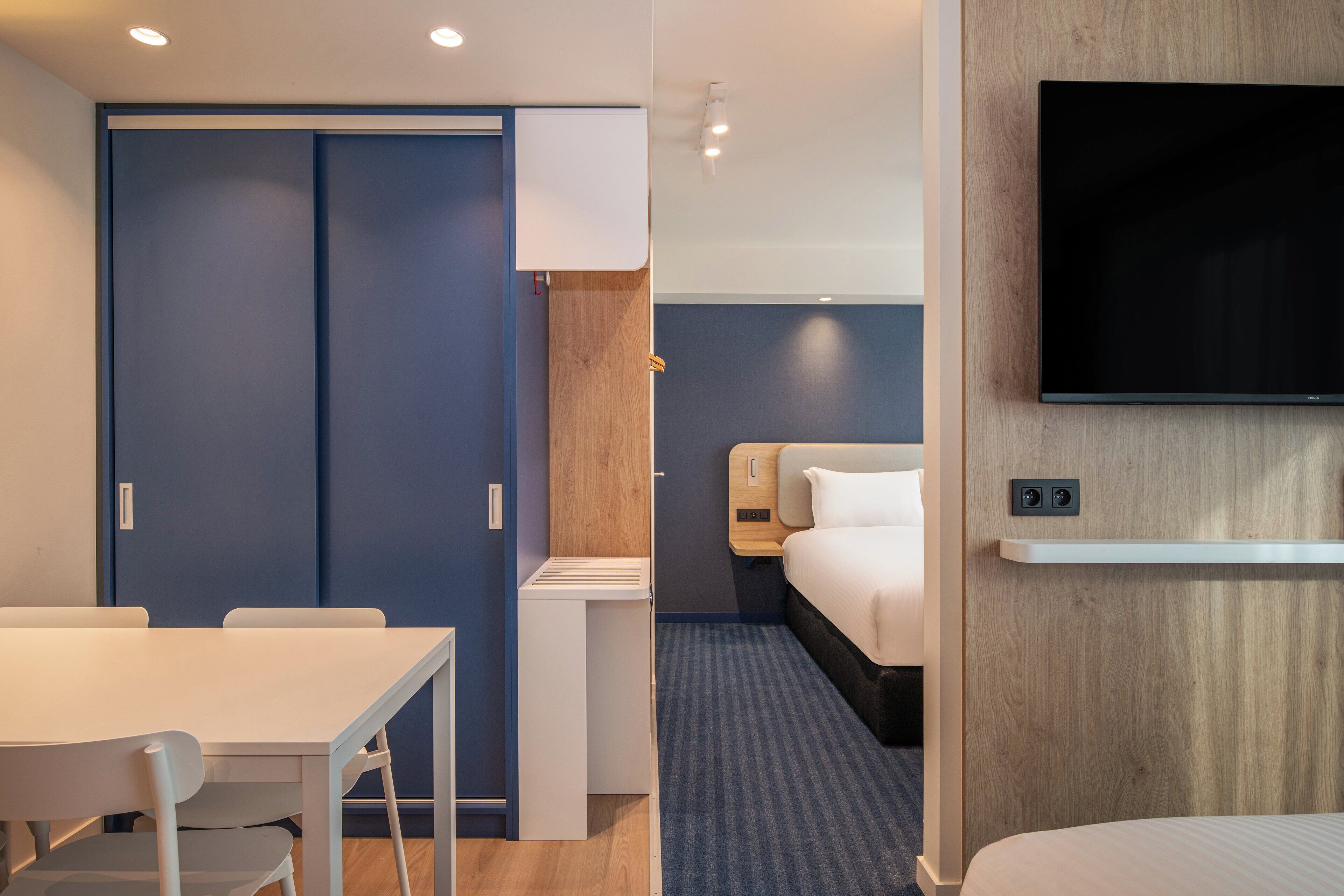 Une chambre d’hôtel comprenant un lit, un téléviseur fixé au mur, un bureau avec une chaise et une armoire.