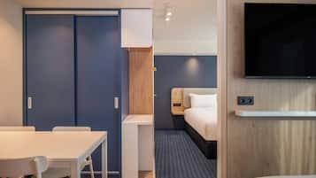 Une chambre d’hôtel comprenant un lit, un téléviseur fixé au mur, un bureau avec une chaise et une armoire.