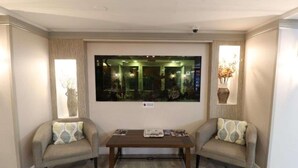 A room with a large mirror, two armchairs, a coffee table, and a vase with dried flowers.