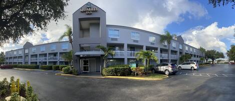A multi-story hotel with a modern design, featuring a prominent lobby area and multiple parking spaces.
