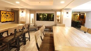 A dining area with wooden tables and chairs, a large painting on the wall, and a view of the outdoors through a window.