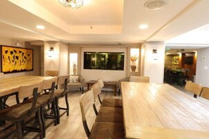 Zona pranzo con tavoli e sedie in legno, un grande quadro appeso al muro e vista sull'esterno attraverso una finestra.