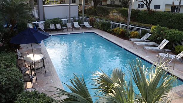 A rectangular swimming pool with a tiled edge, surrounded by white lounge chairs and a few tables.