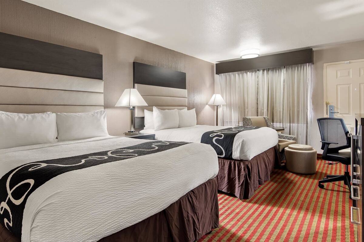 A hotel room with two beds, a desk, a chair, and a television.