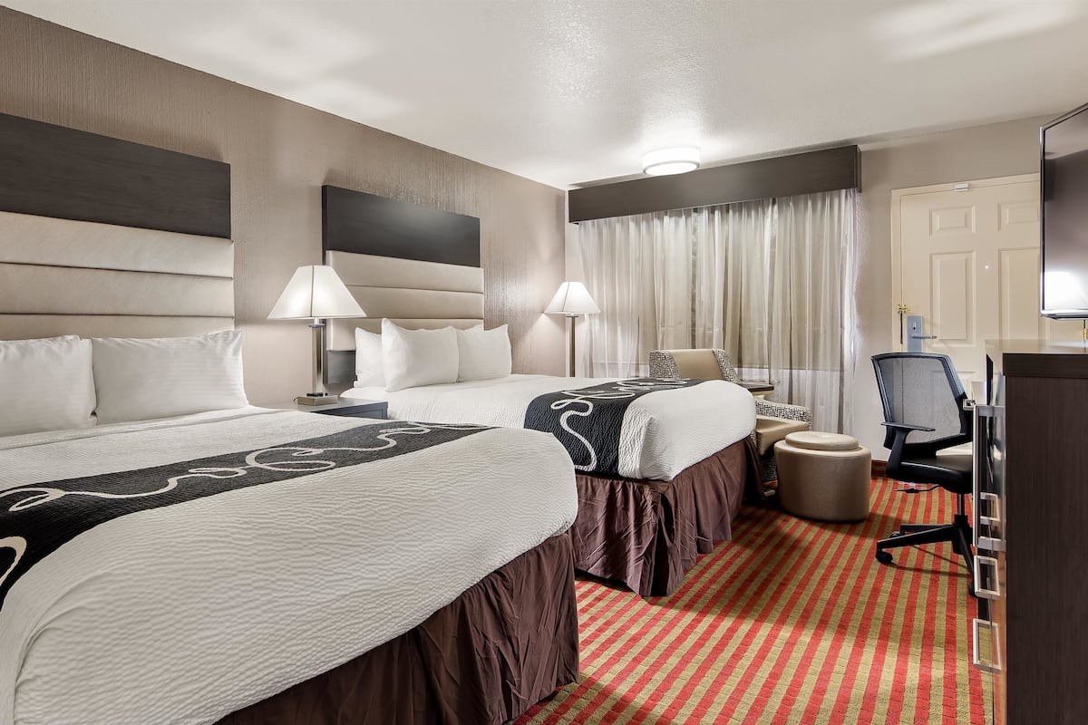 A hotel room with two beds, a desk, a chair, and a TV.