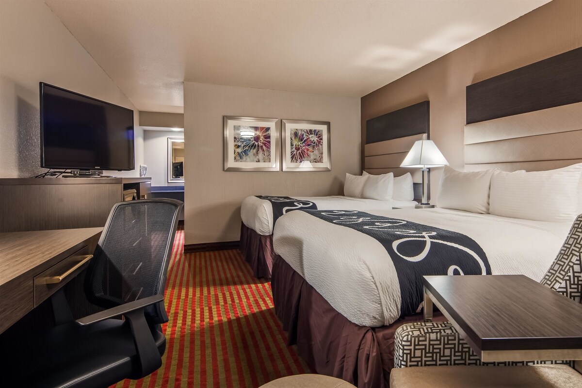 A hotel room with a bed, a desk, a chair, a TV, and two framed artworks on the wall.