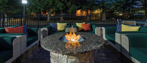 An outdoor seating area with a stone fire pit surrounded by wicker furniture and cushions.