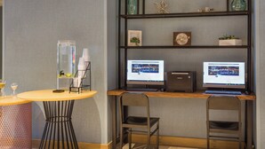 A modern workspace with two computer monitors, a wooden desk, and a round table with a decorative lamp. - Holiday Inn Boone - University Area by IHG (Boone)