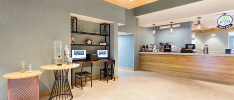 Un interior de cafetería moderna con un mostrador de recepción de madera, zona de estar con mesas y sillas, y una barra con máquinas de café.