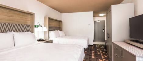 Quarto de hotel com duas camas, televisão, escrivaninha e porta do banheiro.