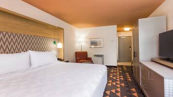 A hotel room with a bed, a chair, a desk, a television, and a wardrobe.