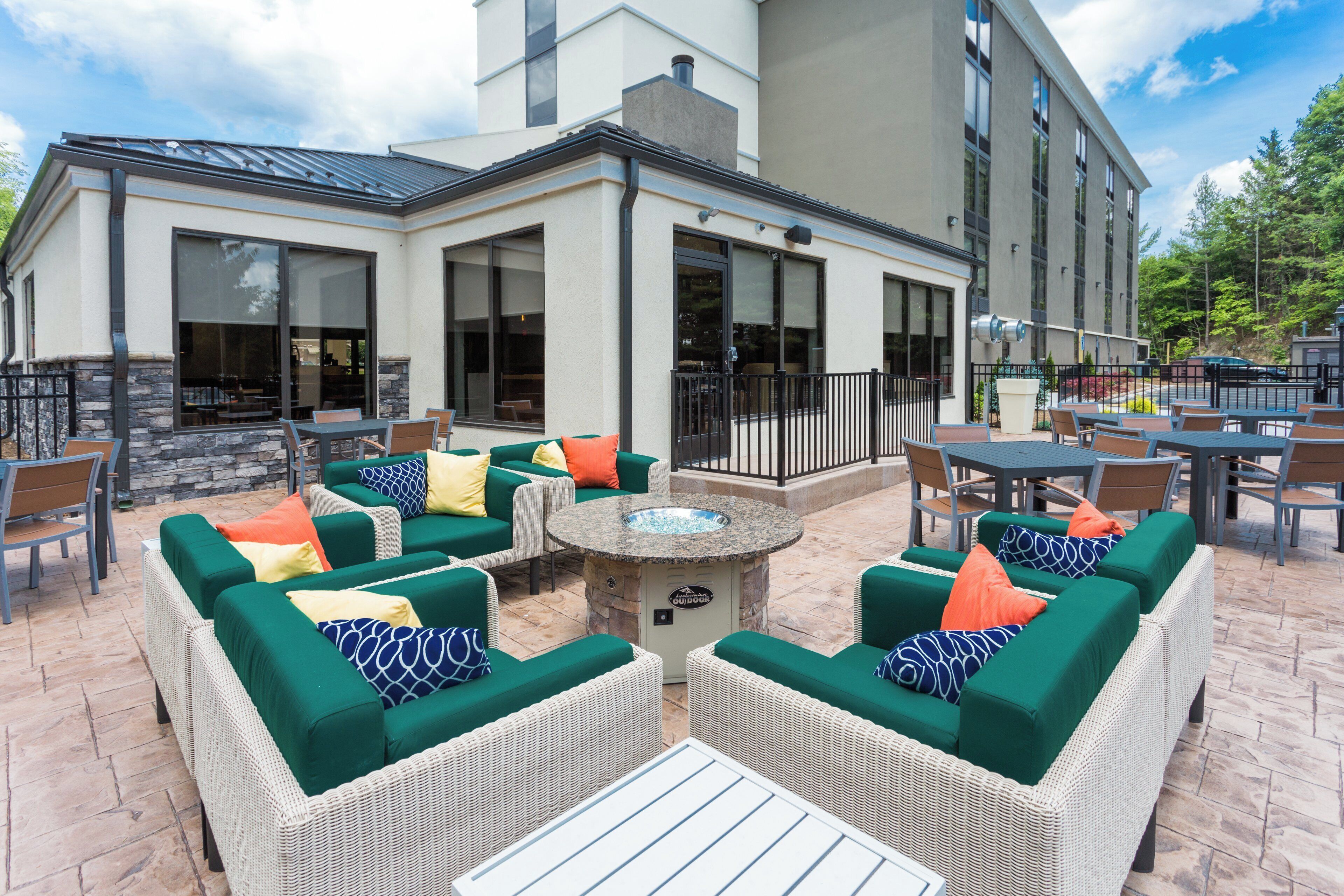 An outdoor patio area with wicker furniture, a fire pit, and a view of the building's exterior.